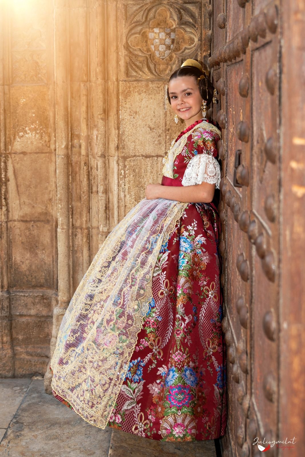 Niña con traje de espolín granate apoyada en una puerta de madera antigua
