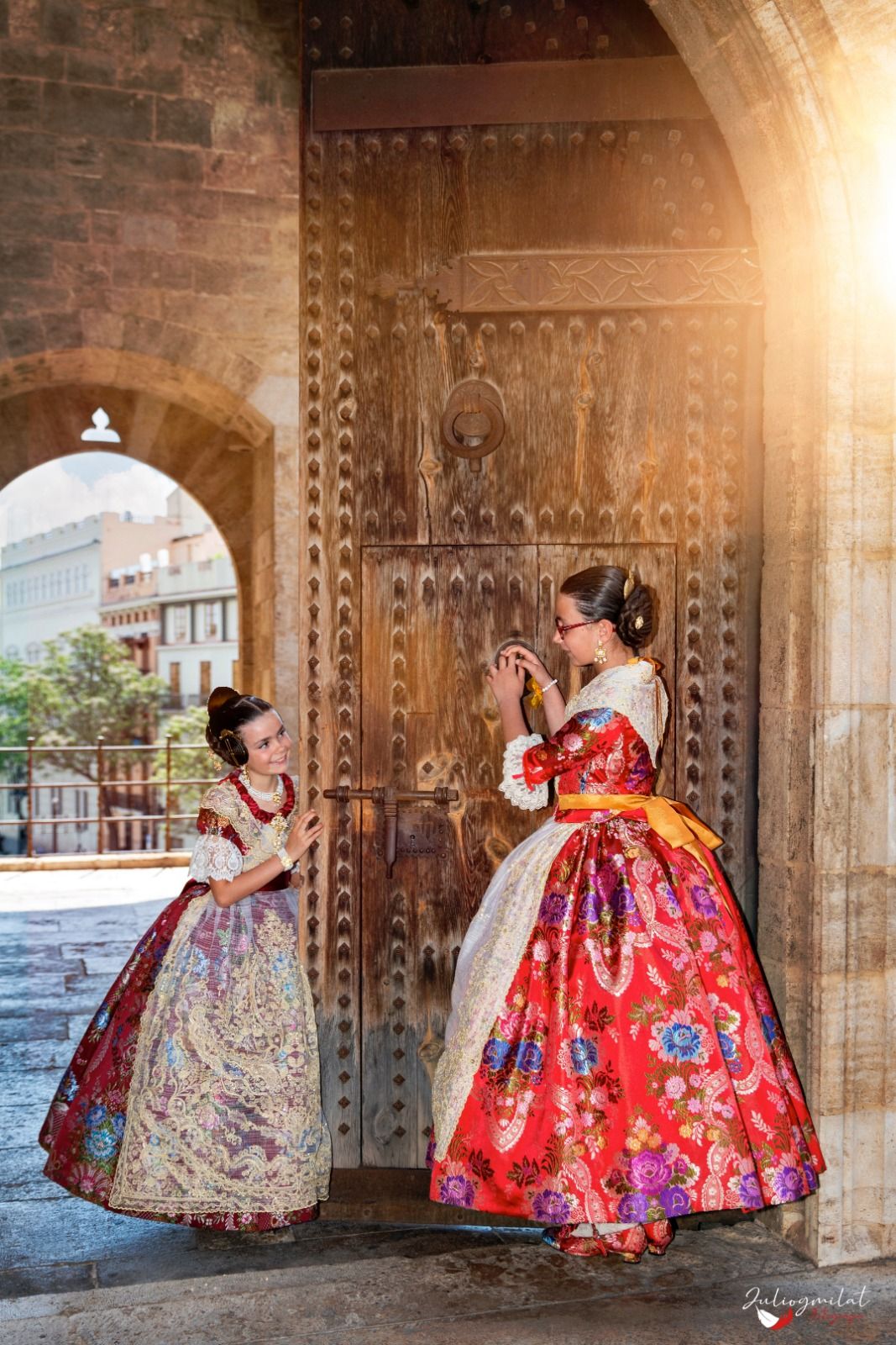 Dos falleras infantiles con trajes de espolín junto a la puerta de madera de las Torres de Serranos