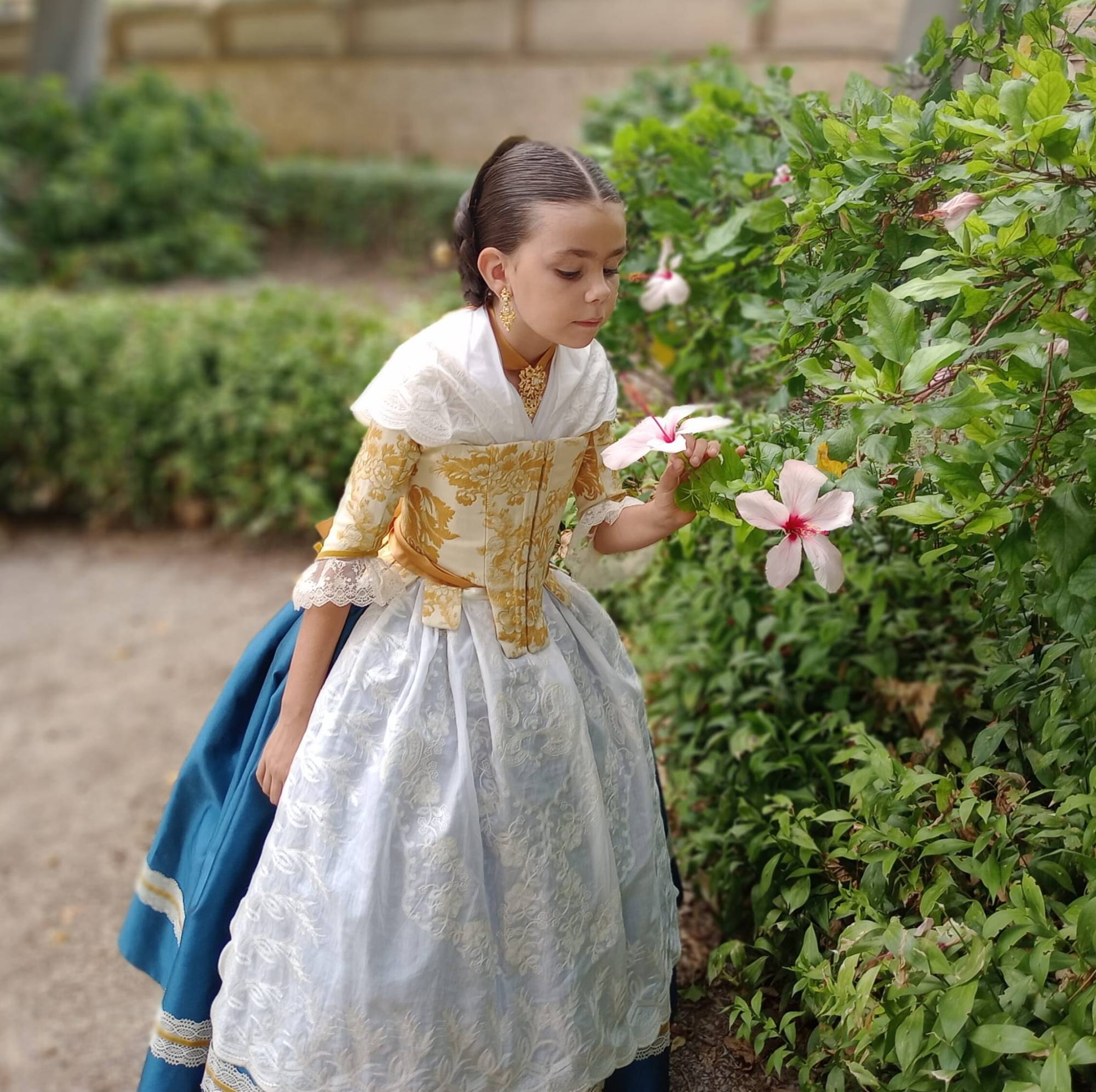 Niña vestida de valenciana oliendo una flor