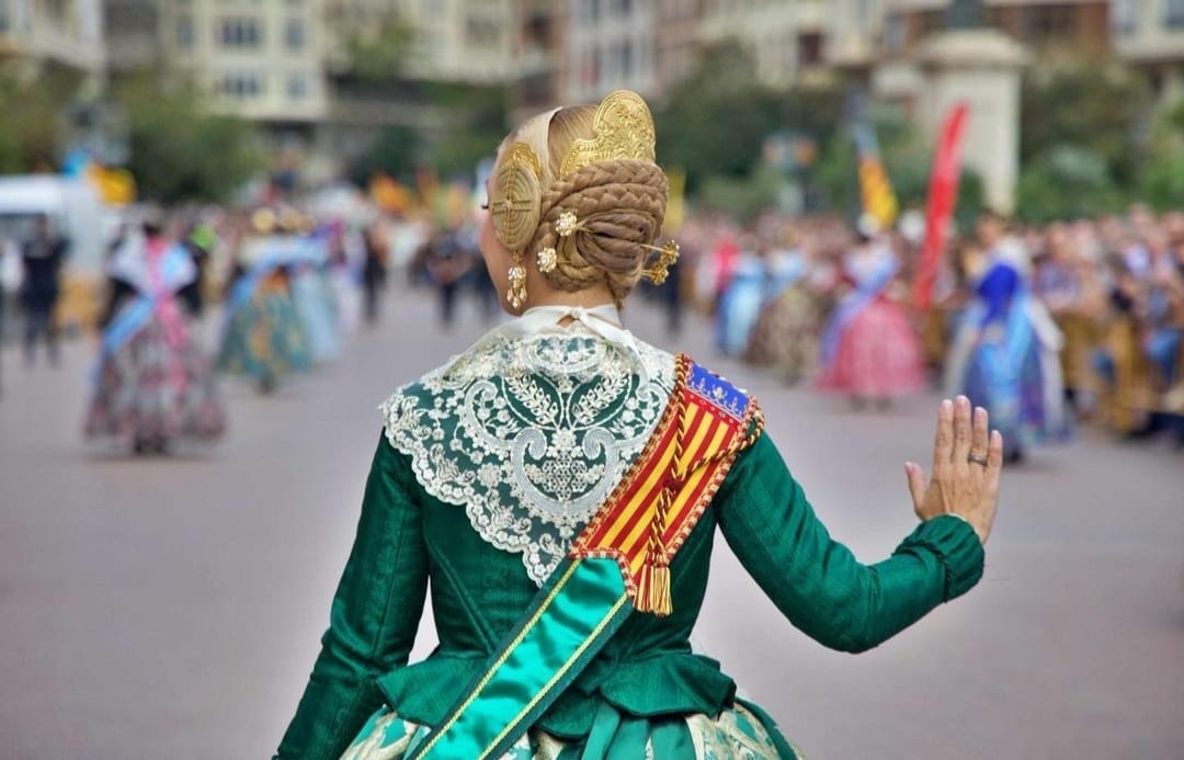 Fallera de espaldas saludando durante la Ofrenda, con manteleta de encaje y traje verde